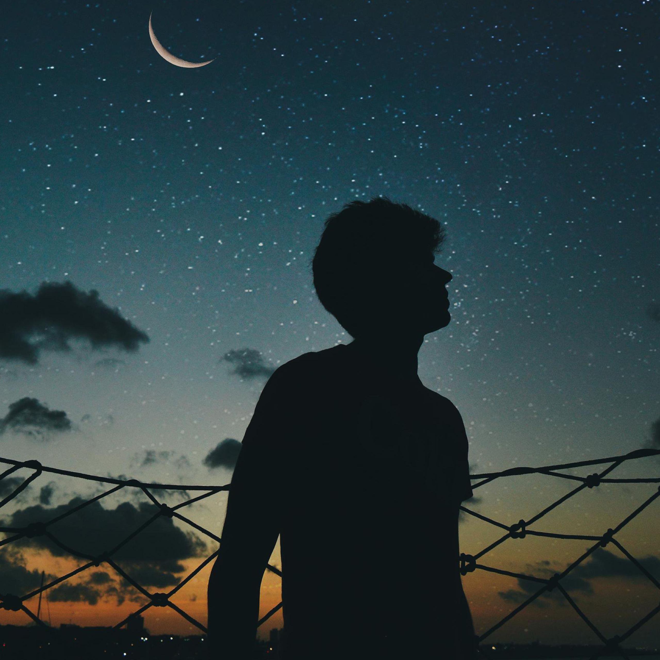 Sziluett egy fiatal férfiről, aki a várostól távol nézi a csillagos eget.
