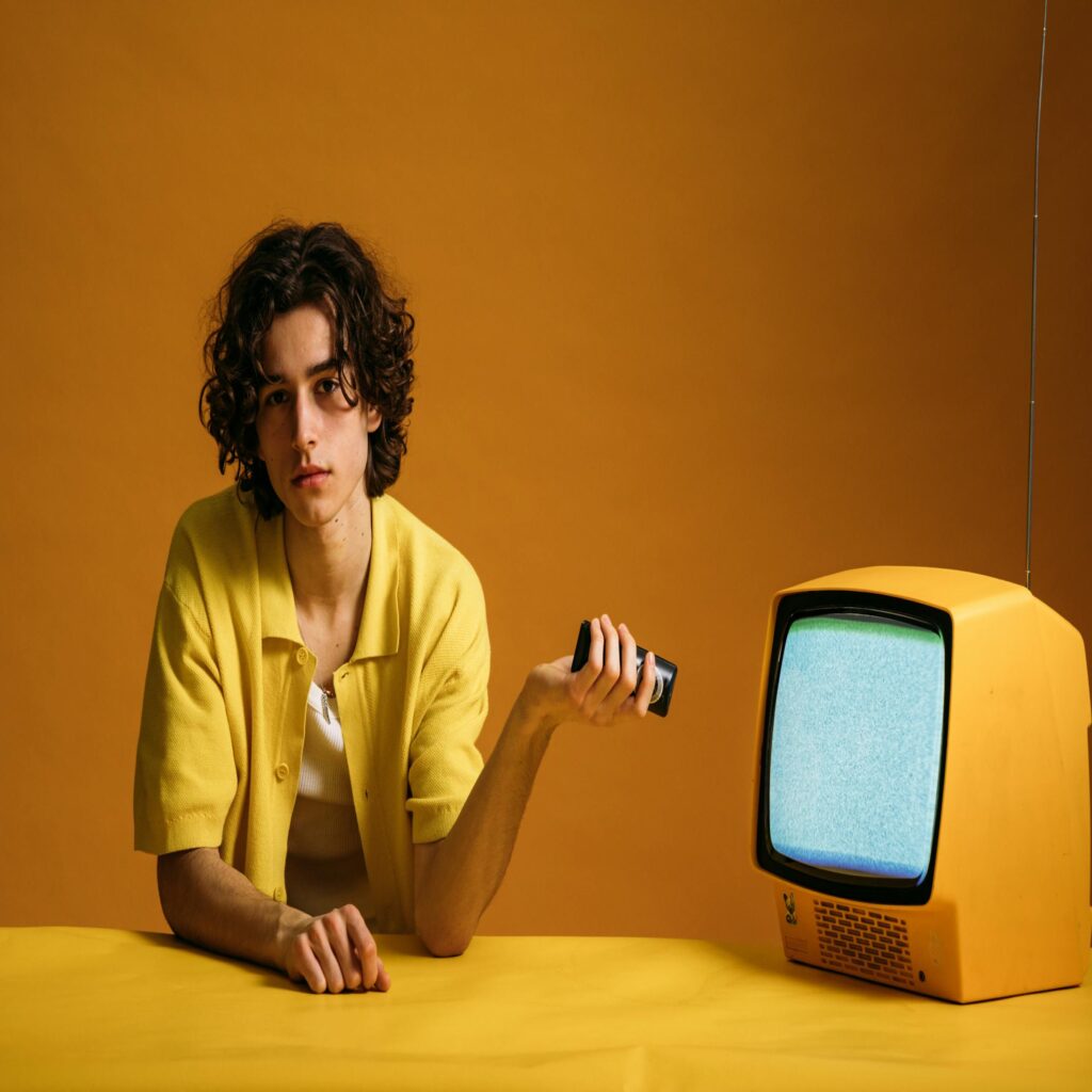 Young man in yellow with a vintage TV in a cool, retro setting.